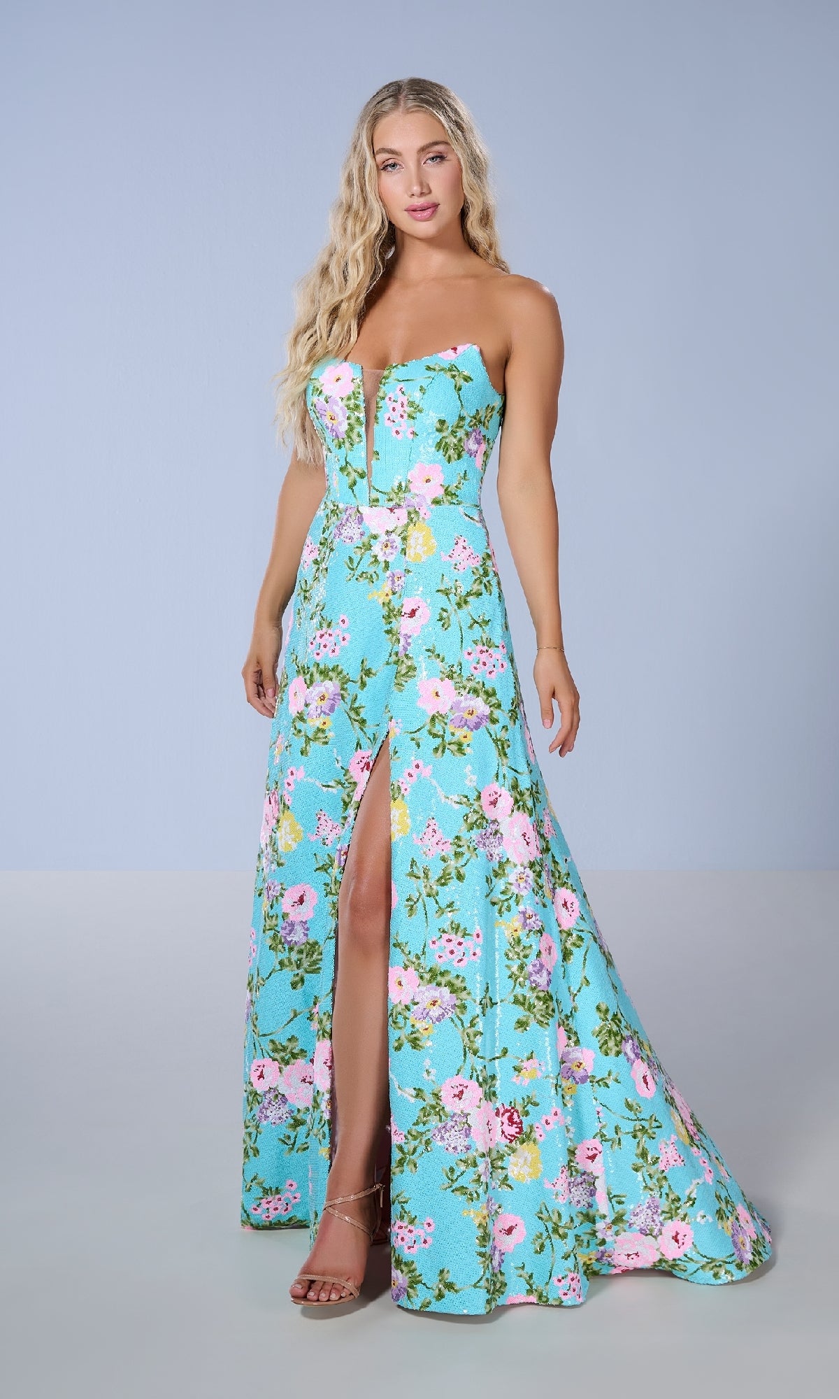 A woman models the Tiffany 16143 long prom dress, a strapless floral gown with a front slit, standing against a plain light blue background.